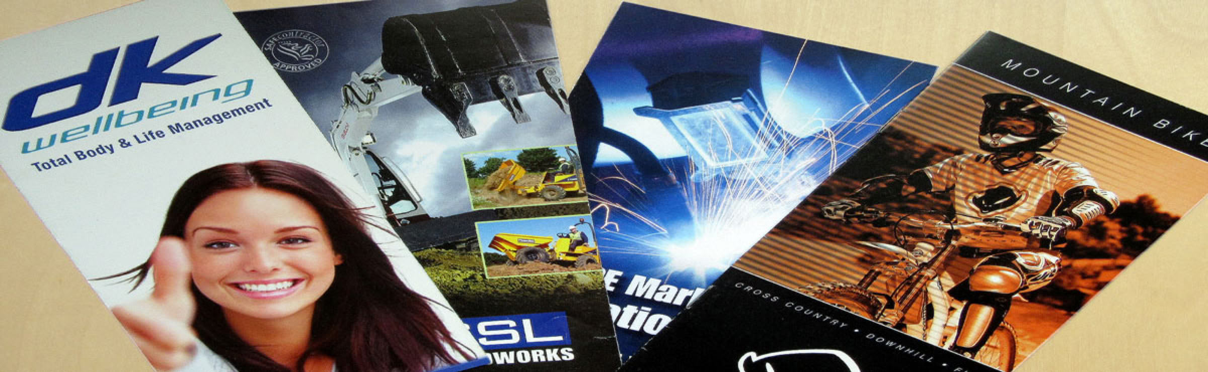 Four brochures arranged in a fan shape on a surface, featuring various images including a smiling person, landscapes, abstract designs, and a person in a racing suit.