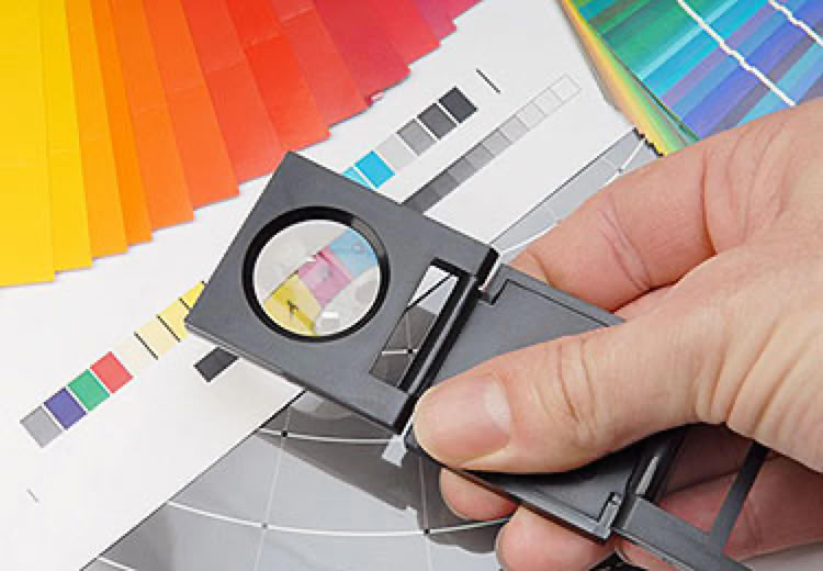 A hand holding a magnifying glass over a color chart with various color swatches and gradients.